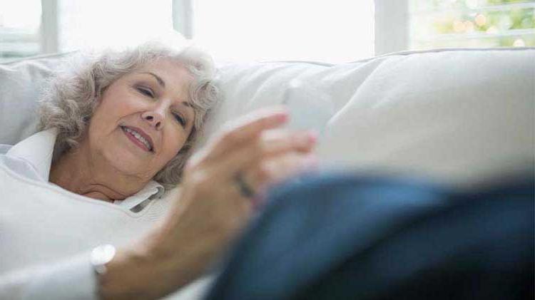 一位老年妇女看着她的便携式设备，检查她的移动健康监测应用程序.