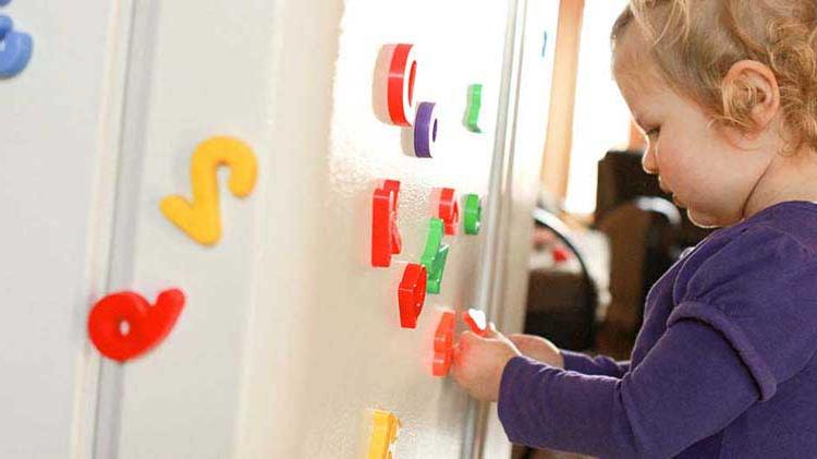 Toddler playing with refrigerator magnets that could cause a household hazard.