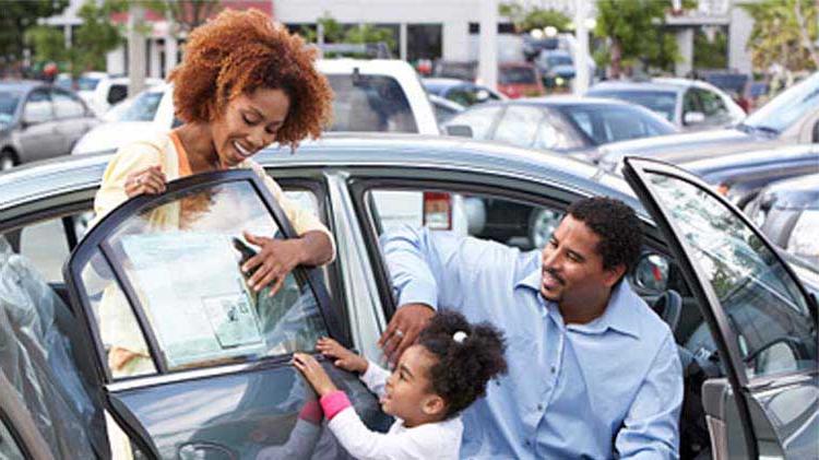 A family is looking at a used car on a dealership lot.