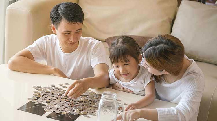 Family of three sitting around a table with coins poured out from a jar.