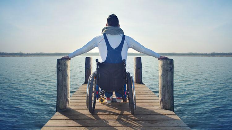 一个残疾人坐在轮椅上，站在码头上俯瞰湖面.