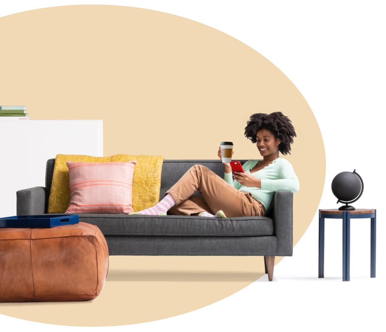 Woman sitting on couch holding a coffee while reading her iPhone about what renters insurance covers. A globe sits on side table.